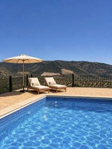 a swimming pool with two chairs and an umbrella at Cortijo Sol y Olivo spacious exclusive private pool retreat in Algarinejo