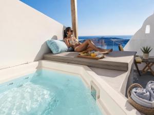 a woman sitting on a couch next to a swimming pool at Cliff Caldera Modern Suites -Volcano, Sunset & Caldera View in Fira