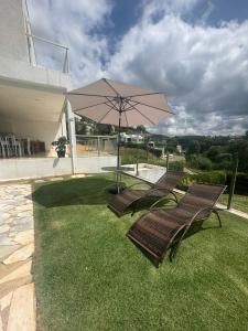two chairs and a table with an umbrella on a lawn at Pousada da Esdras in Capitólio
