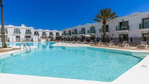 a pool with chairs and palm trees in front of a hotel at NEW AVATEA Parque Natural, piscinas y tennis in Corralejo
