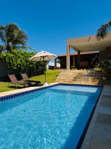 a swimming pool with an umbrella next to a house at Casa Paraíso Guajiru in Trairi