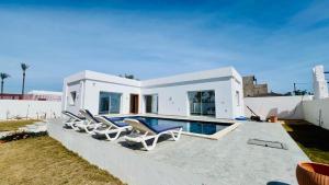 a white villa with a swimming pool and lounge chairs at Corail in Djerba