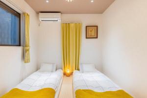 two beds in a room with yellow curtains and a window at nonon in Osaka