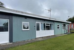 a green building with white doors and a yard at Cosy Cabin in Bucks Mills