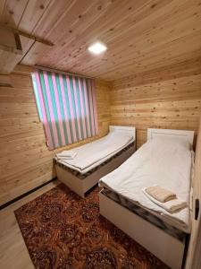 two beds in a wooden room with a window at Naryn Barnhouses in Naryn