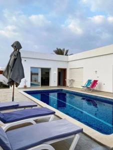 a swimming pool with chairs and an umbrella next to a house at Corail in Djerba