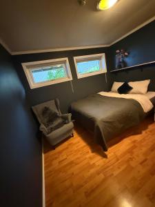 a bedroom with a bed and a chair and two windows at Cozy apartment with two bedrooms in Tromsø