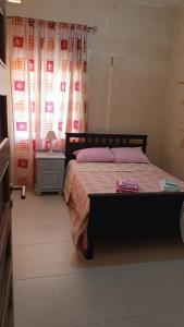 a bedroom with a bed and a table and curtains at Tan-Nahal Court Apartment, Sannat Gozo in Sannat