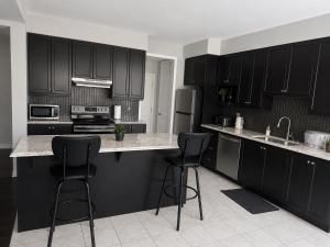 a kitchen with black cabinets and two bar stools at Gifted Beautiful Home in Brampton