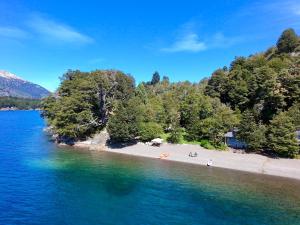 a beach with trees on the shore of a lake at Apart Hotel La Busqueda in Moquehue