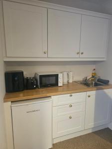 a kitchen with white cabinets and a microwave and a sink at Mini studio apartment in Tulla