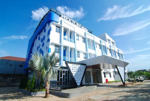 a blue and white building with a palm tree in front at Hexton Hotel Lampung in Tanjungkarang