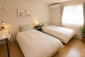 two beds in a room with a desk and a window at ゲストハウスガーデンズmihama in Wada