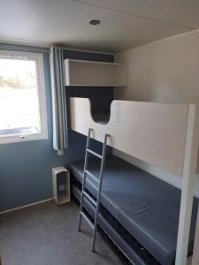 a bunk bed with a ladder in a room with a window at Mobil home 3ch, clim, bord de mer in Seignosse