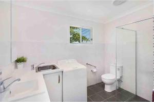 a white bathroom with a toilet and a sink at Kingscliff Spacious Beach Cottage in Kingscliff +13 photos