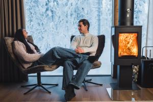 a man and woman sitting in chairs in front of a fireplace at Wilderness Hotel Saariselkä in Saariselka