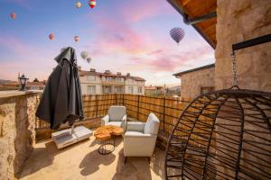 a balcony with chairs and an umbrella and hot air balloons at Cappadocia Tughan Stone House in Uçhisar