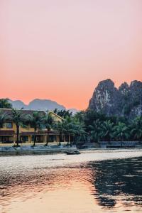 a house on the water with mountains in the background at Le Maison Tam Coc Boutique Hotel in Ninh Binh