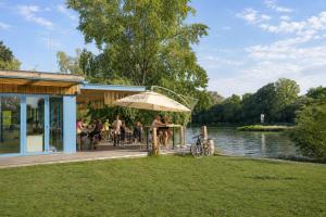 a group of people sitting at a table on a deck next to a lake at Apartmány park in Poděbrady