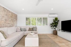 a white living room with a couch and a tv at The Bower - Byron Hinterland in Teven