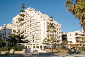 a white building with palm trees in front of it at Hotel Helios Costa Tropical in Almuñécar
