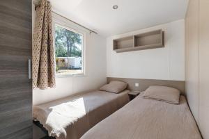 two beds in a small room with a window at Bungalow Cap Ferret Les Lodges 3 in Lège-Cap-Ferret