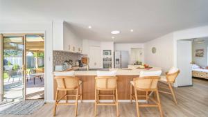 a kitchen with white walls and wooden floors and a bar with chairs at Salt n Sand Beach house - 10min walk to Ocean - Idyllic coastal village in Ocean Shores