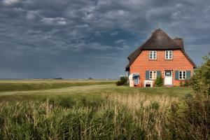 a large red brick house with a thatched roof in a field at Haus Nordmarsch in Langeneß