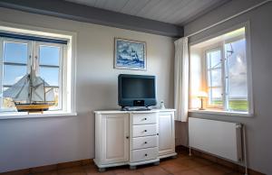 a room with a tv on a dresser with two windows at Haus Nordmarsch in Langeneß