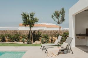 a patio with two chairs and a table and a pool at Canalola in Cala en Bosc