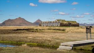 a field with a bridge and a building in the distance at Fjalladýrð Hotel in Modrudalur