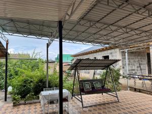 a porch with a swing and a table under a roof at Shabdan Guest House in Toktogul