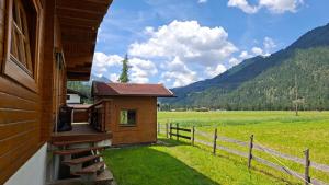 a building with a porch next to a field and a fence at Chalet am Lechweg in Elbigenalp