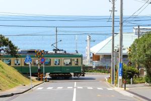 a green train traveling down a street next to the ocean at 湘南で暮らすように泊まる一棟貸し U-house Shonan in Fujisawa +29 photos