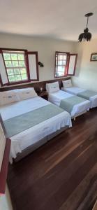 three beds in a room with wood floors and windows at Pousada dos Bandeirantes in Ouro Preto