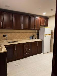 a kitchen with wooden cabinets and a white refrigerator at الشهداء الفاخر للشقق المخدومة in Medina