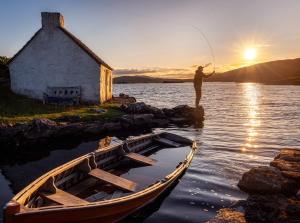 a man fishing in the water next to a boat at Carraroe Apartment in Carraroe