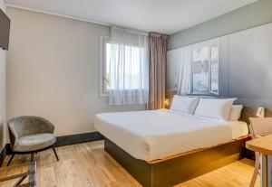 a hotel room with a bed and a chair at B&B HOTEL Bordeaux Sud Mios 3 étoiles in Mios