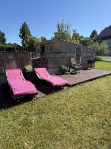 two pink cushioned chairs on a patio in a yard at Английский домик in Lapmežciems