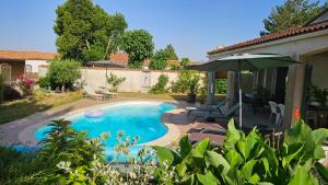 a swimming pool with an umbrella and a house at GITE familiale avec piscine in Saint-Martin-de-la-Coudre