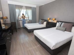 a woman standing in a hotel room with two beds at Mercure Santiago Centro in Santiago