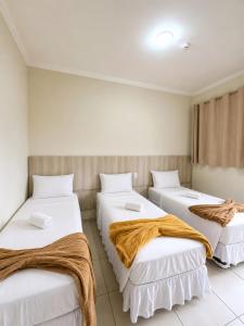 three beds in a room with white sheets at Glória Hotel in Olímpia