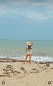 a woman in a hat standing on the beach at CASTLE WHITE by MONARCA in Ríohacha