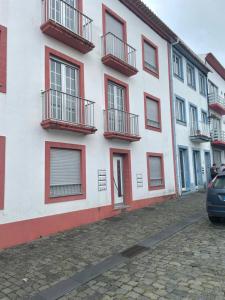 a white building with red balconies on a street at Refúgio Das Ondas in Praia da Vitória