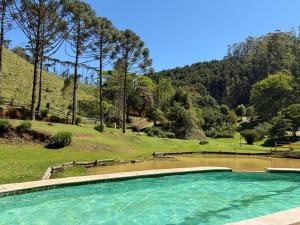 a swimming pool in front of a hill with trees at Pousada A Casa da Fazenda in Santo Antônio do Pinhal
