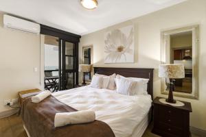a bedroom with a large white bed and a mirror at Luxury Ocean View 1203 with Workspace, AC & Beachfront Location in Cape Town