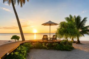 two chairs and an umbrella on the beach at sunset at Aitutaki Escape Resort & Spa in Arutanga