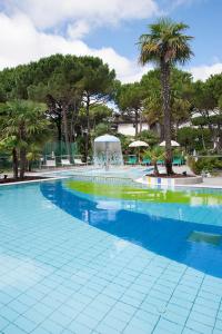 a large swimming pool with palm trees and a fountain at Hotel Delle Nazioni in Lignano Sabbiadoro