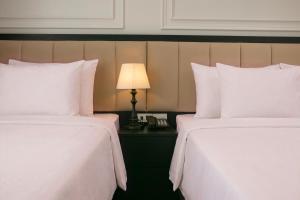two beds with white sheets and a lamp on a table at Euphoria Hotel & Spa in Hanoi