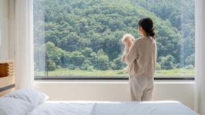 a woman holding a teddy bear looking out a window at Hongcheon Around River Poolvilla Pension in Mangdani